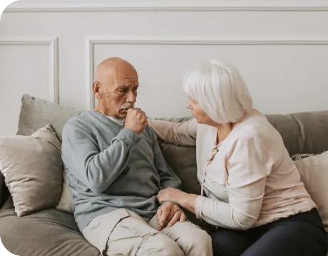 Elderly man coughing while supported by his wife, representing chest wall tumour symptoms